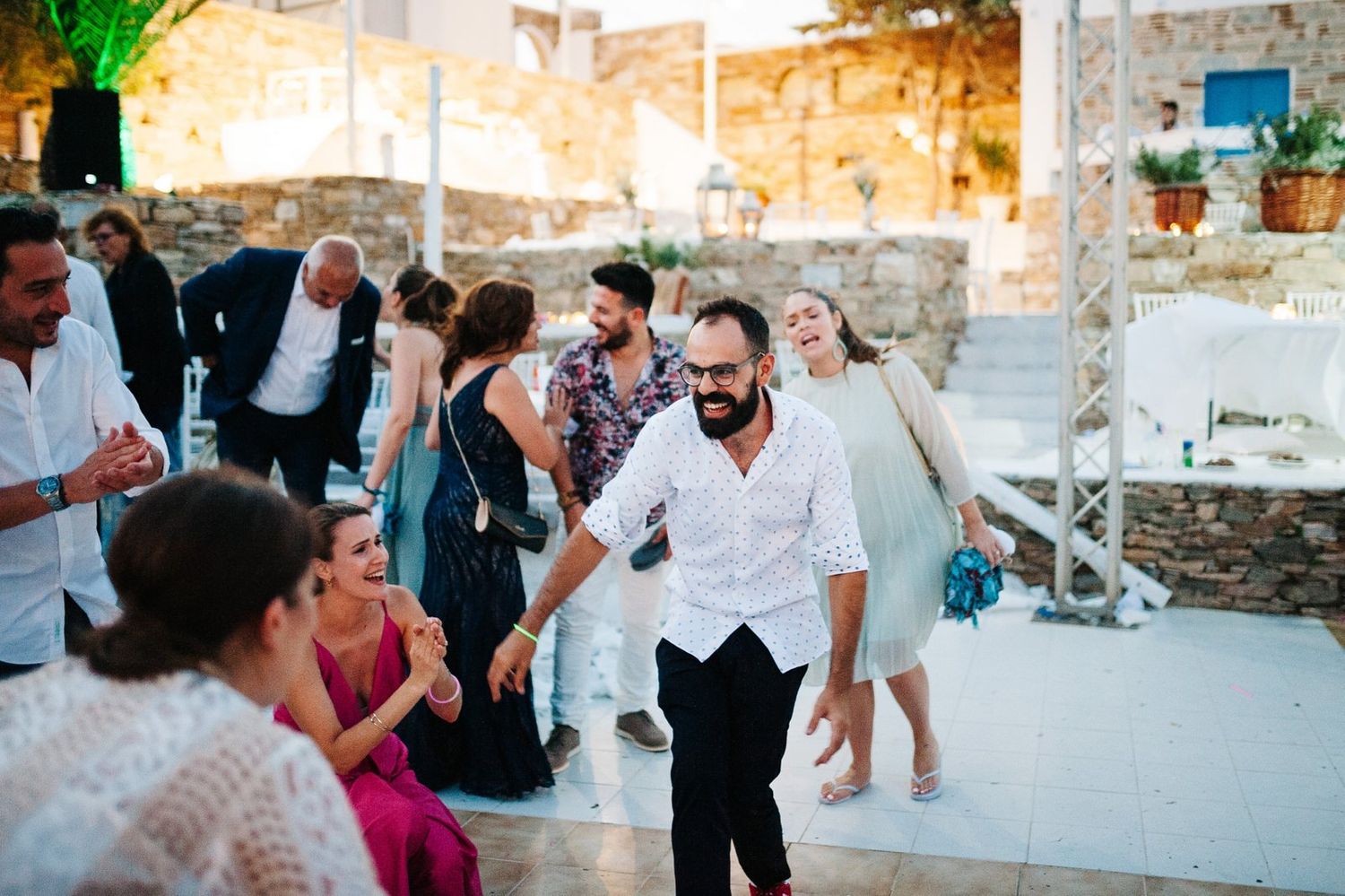 Wedding guests dancing and socializing at an outdoor stone-walled venue.