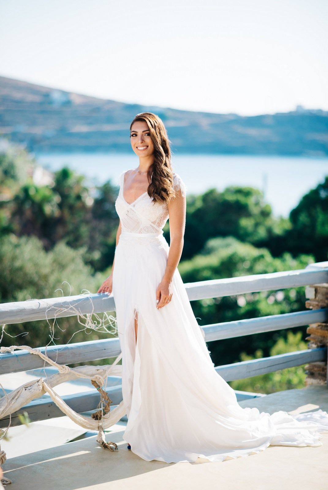 A white wedding dress on a scenic balcony overlooking a coastal landscape with mountains and water in the background.
