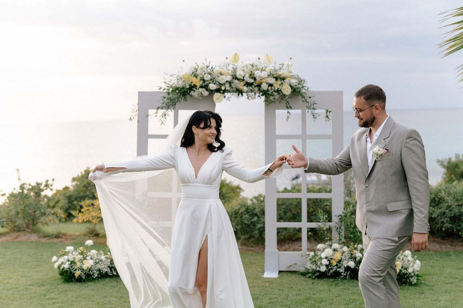 A romantic outdoor beach wedding ceremony with white floral arrangements and a flowing bridal veil catching the ocean breeze.