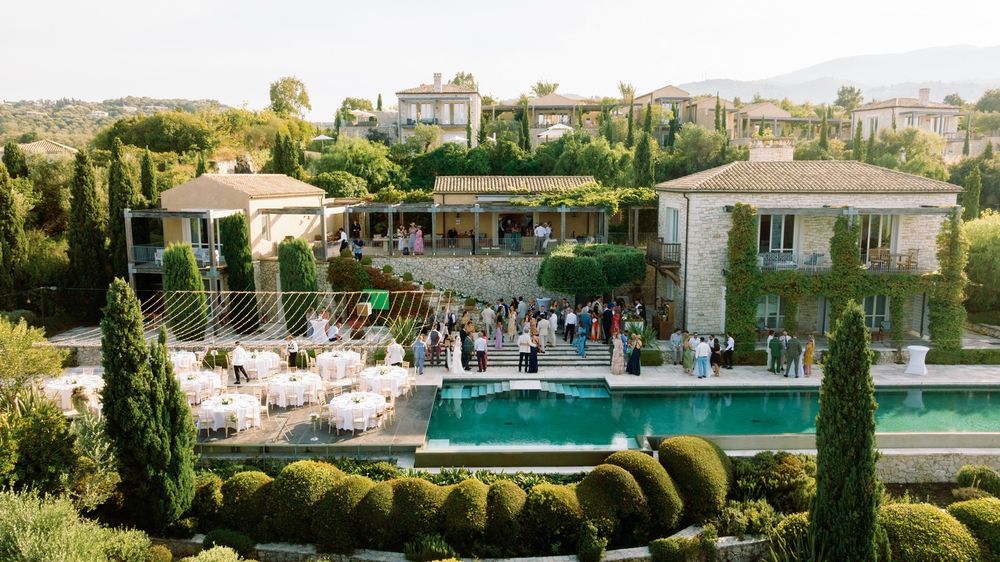 Luxury Mediterranean villa with a turquoise pool and manicured cypress gardens overlooking a scenic landscape.