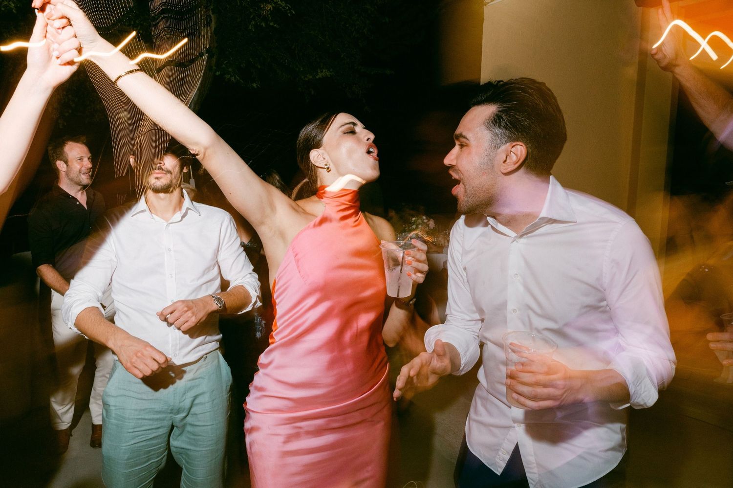 People dancing energetically at a party with festive lighting in the background.