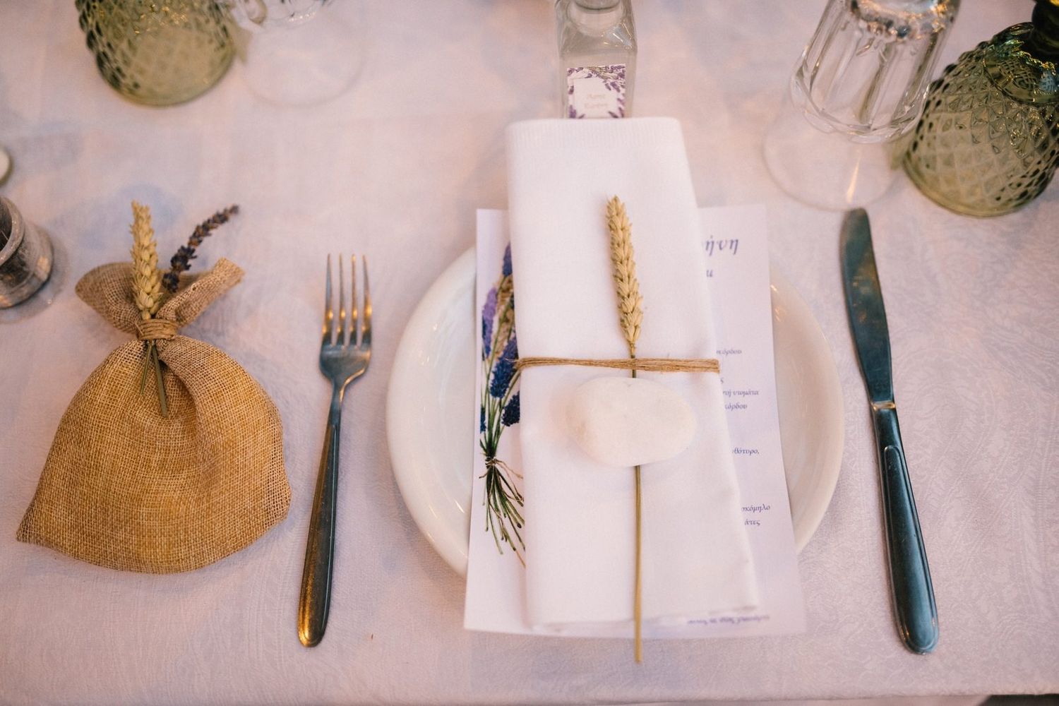 Rustic wedding place setting with wheat stalks and burlap accents on white dinnerware.