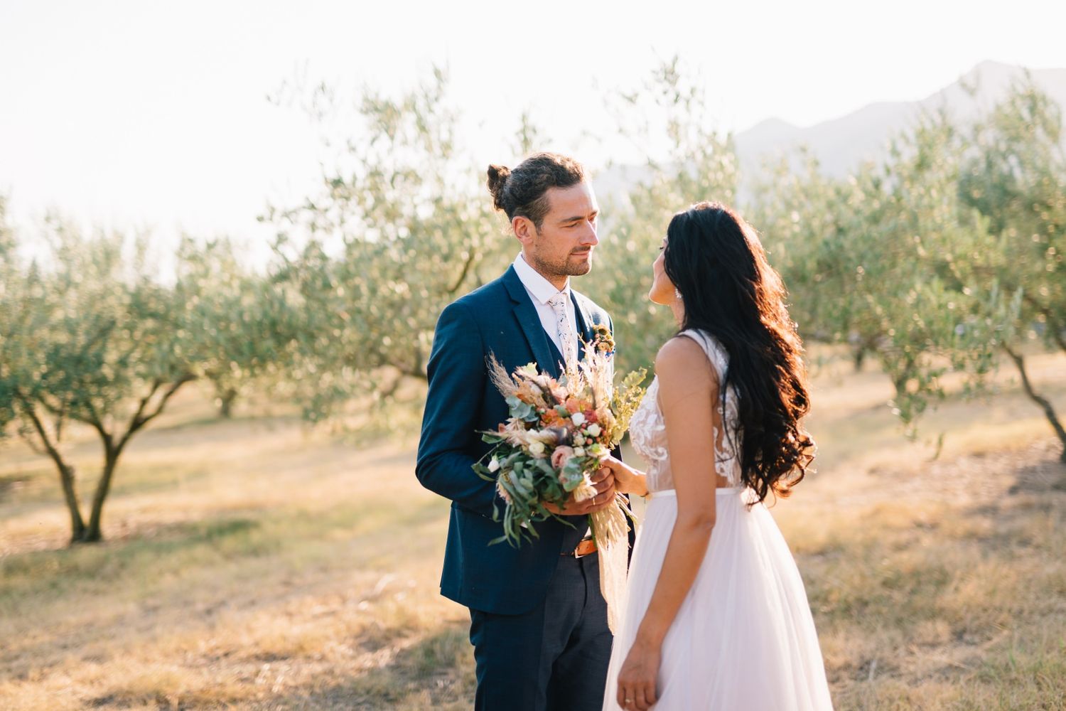 Romantic couple standing among olive trees in golden afternoon light.