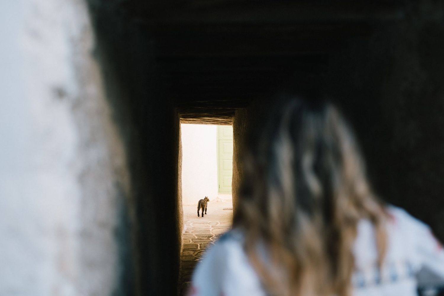 A blurred figure in the foreground looking through a narrow passageway at a distant doorway.