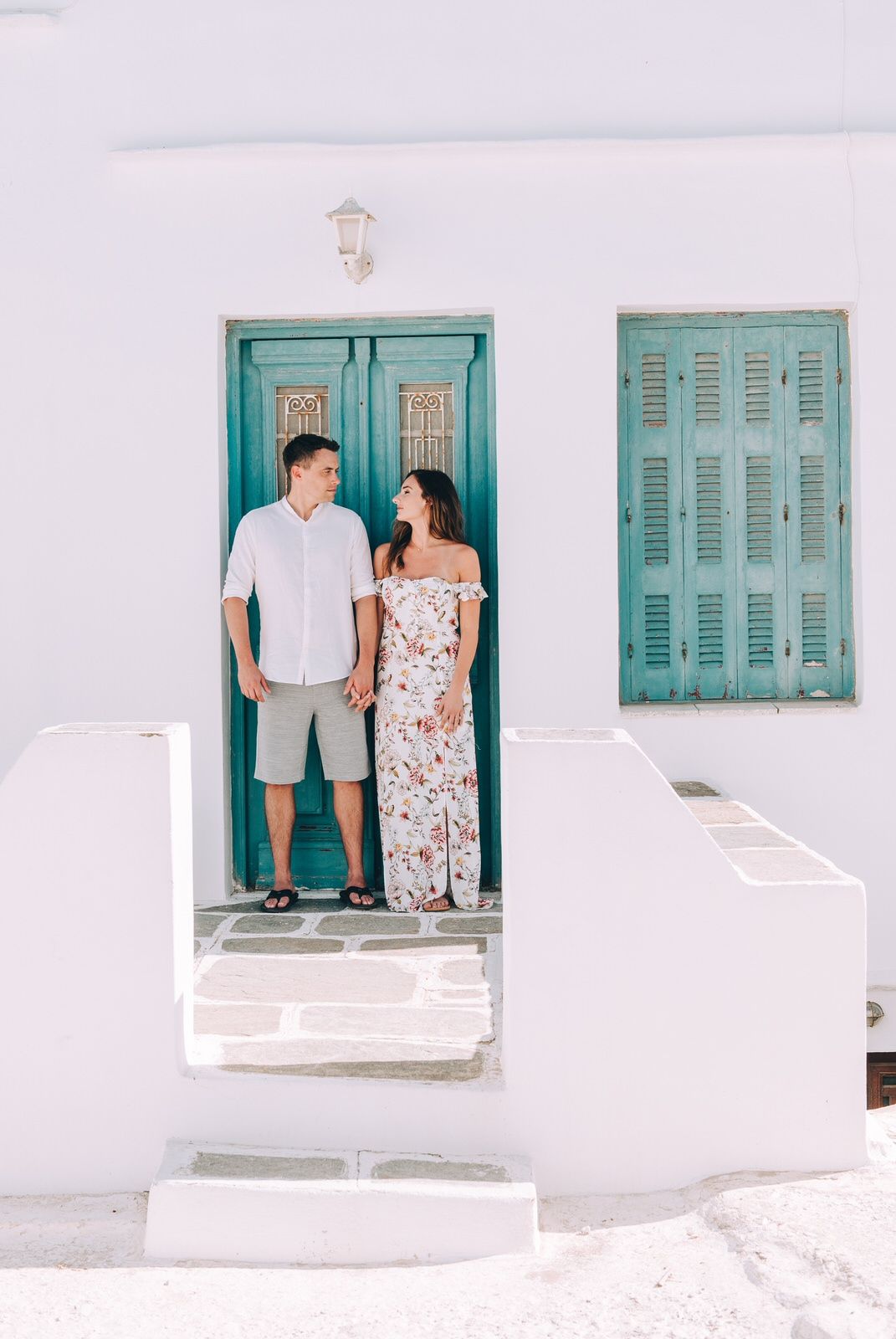 A bright Mediterranean doorway with turquoise shutters and white walls creating a classic Greek island aesthetic.