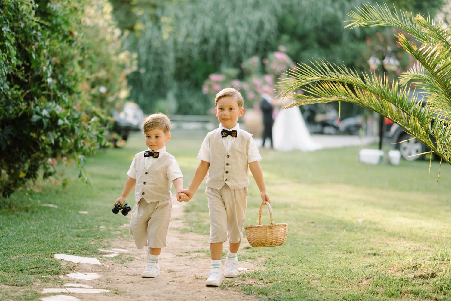 Two young ring bearers in light beige suits walking down a garden path.