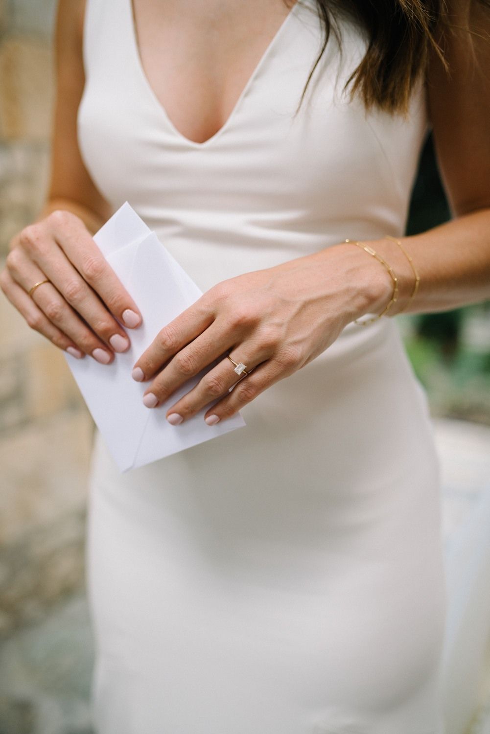 Close-up of hands holding a letter while wearing an elegant white wedding dress.