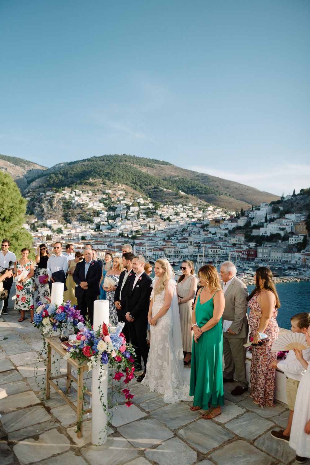 Scenic destination wedding overlooking Mediterranean hillside town with guests and floral decor.