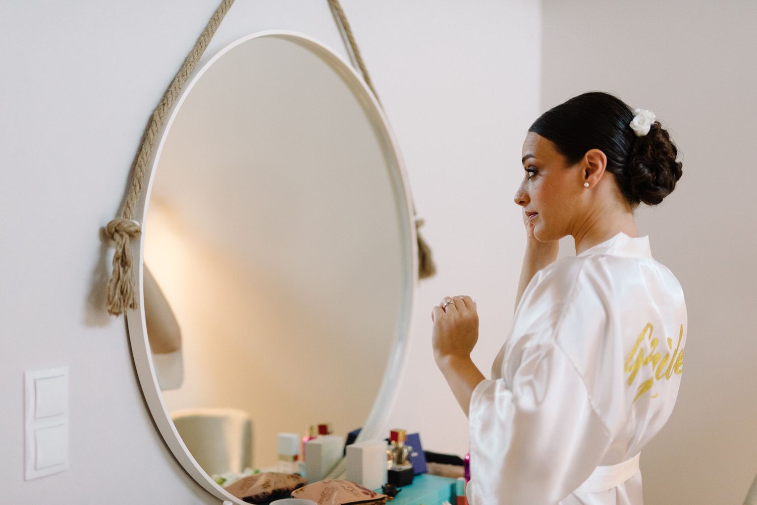 A person in a white robe looks in a round mirror during wedding preparations.
