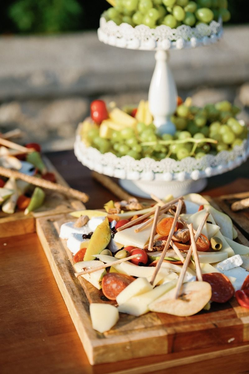 Elegant tiered display of fresh grapes and appetizers on wooden serving board at outdoor event.
