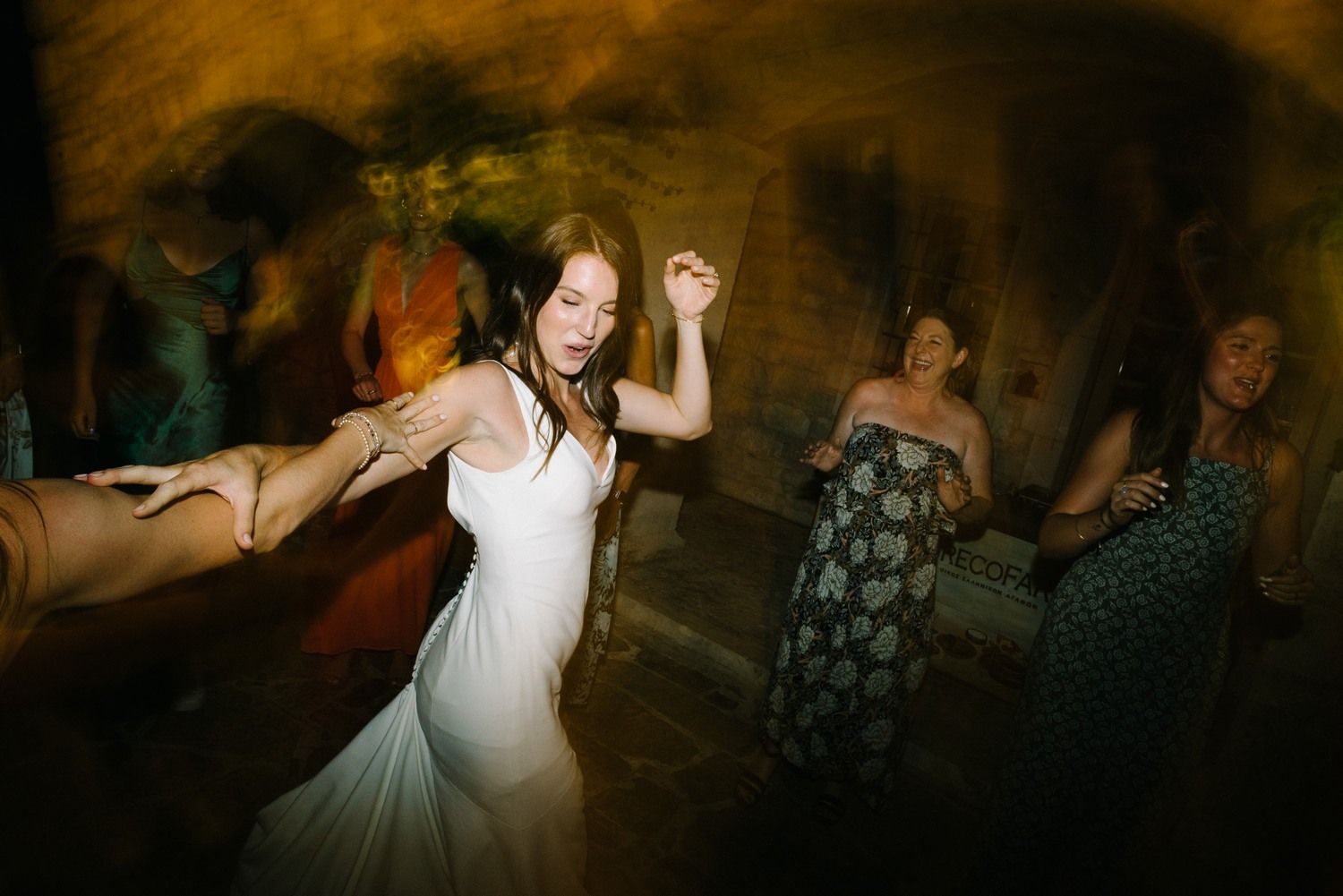 A woman in a white dress dances joyfully at a dimly lit reception venue.