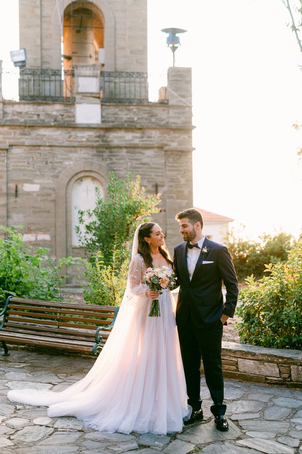 A romantic wedding couple shares intimate moments in front of a stone church during golden hour.