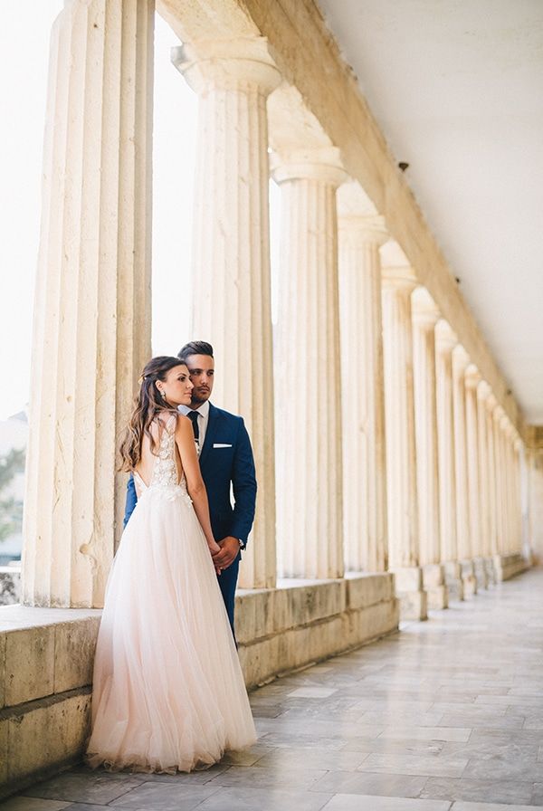 A bride and groom share an intimate moment among elegant stone columns in a classical architectural setting at corfu island.