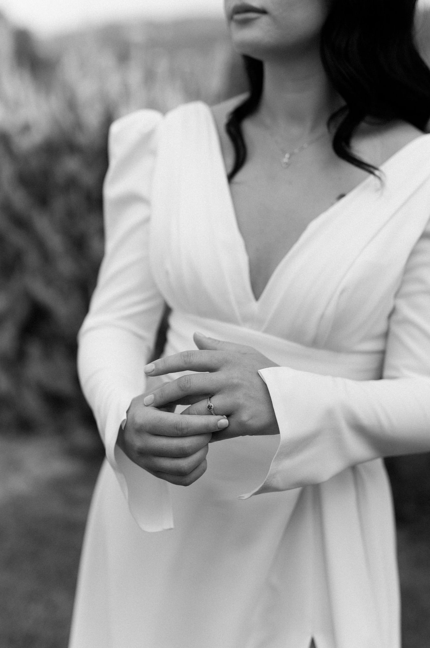 Black and white close-up of a white wedding dress with long sleeves and a delicate neckline, showing clasped hands.