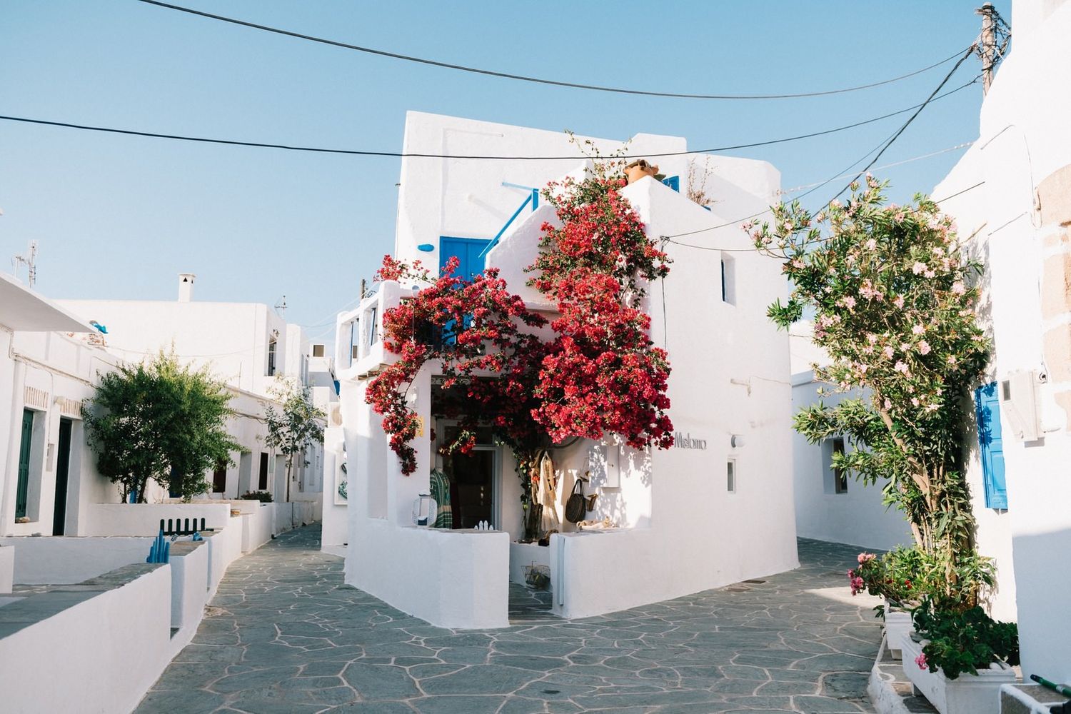 White coastal buildings with ocean views nestled on Greek hillside under blue sky.