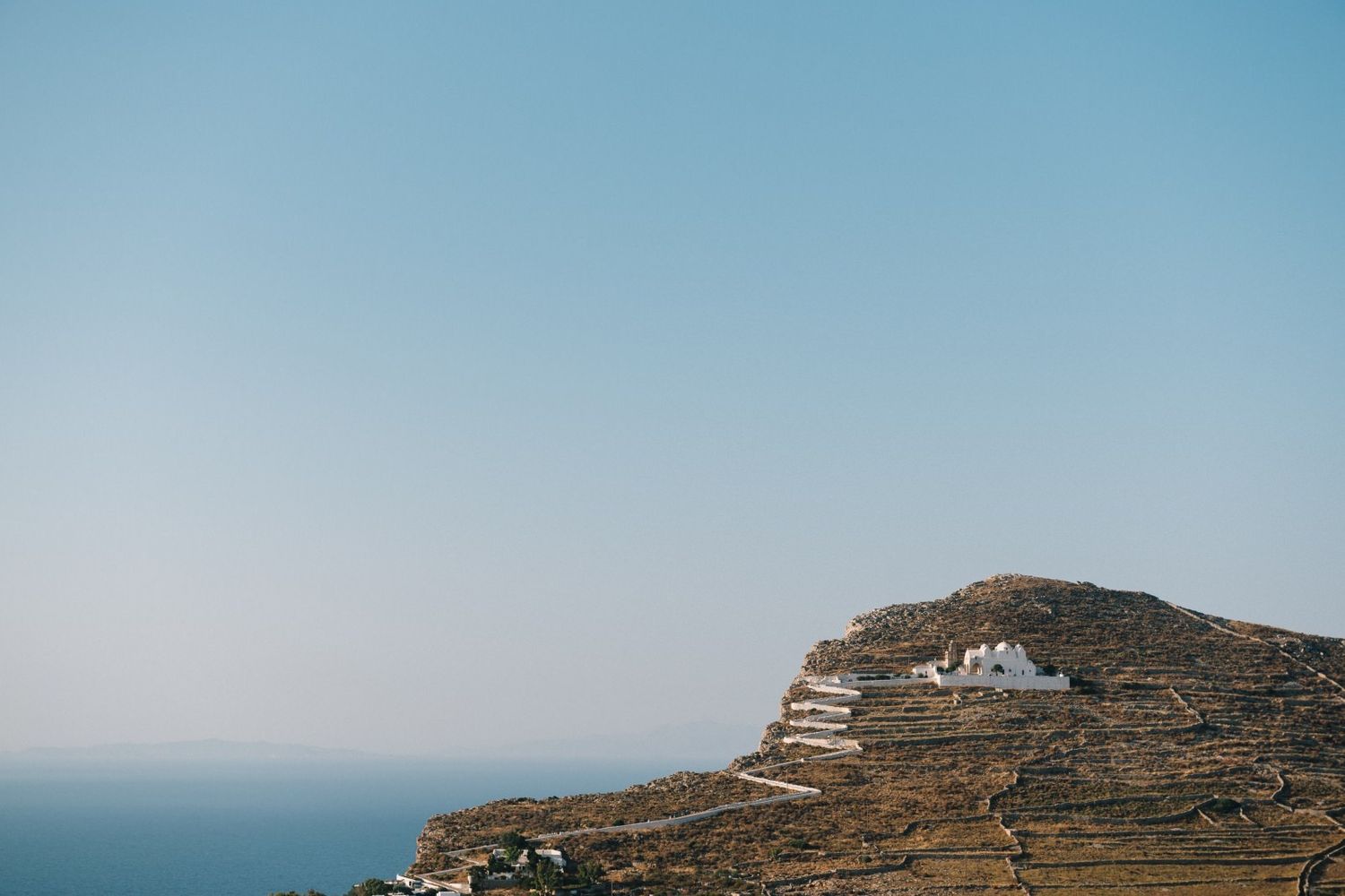 Scenic view of Greek island with white church perched on mountainside overlooking ocean.