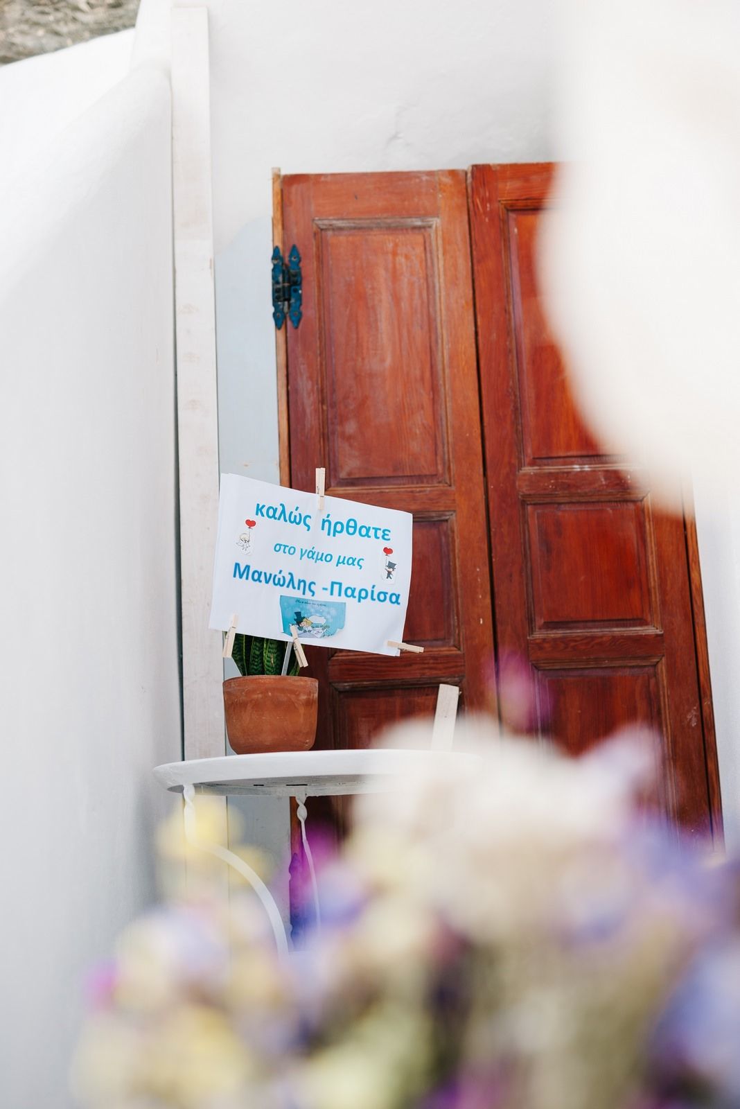 Rustic wooden door with Greek signage and purple flowers in foreground.