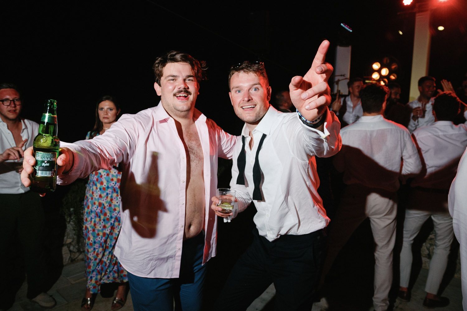 Party guests celebrating with drinks at nighttime outdoor event with white attire.