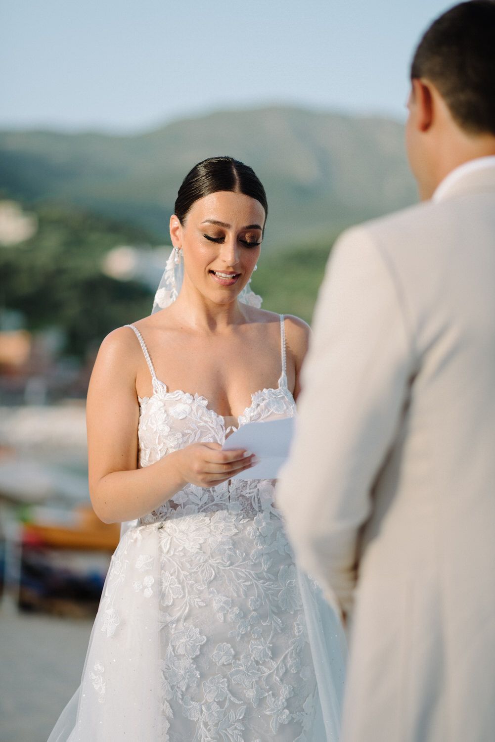 Bride in lace wedding dress reading vows during outdoor ceremony.