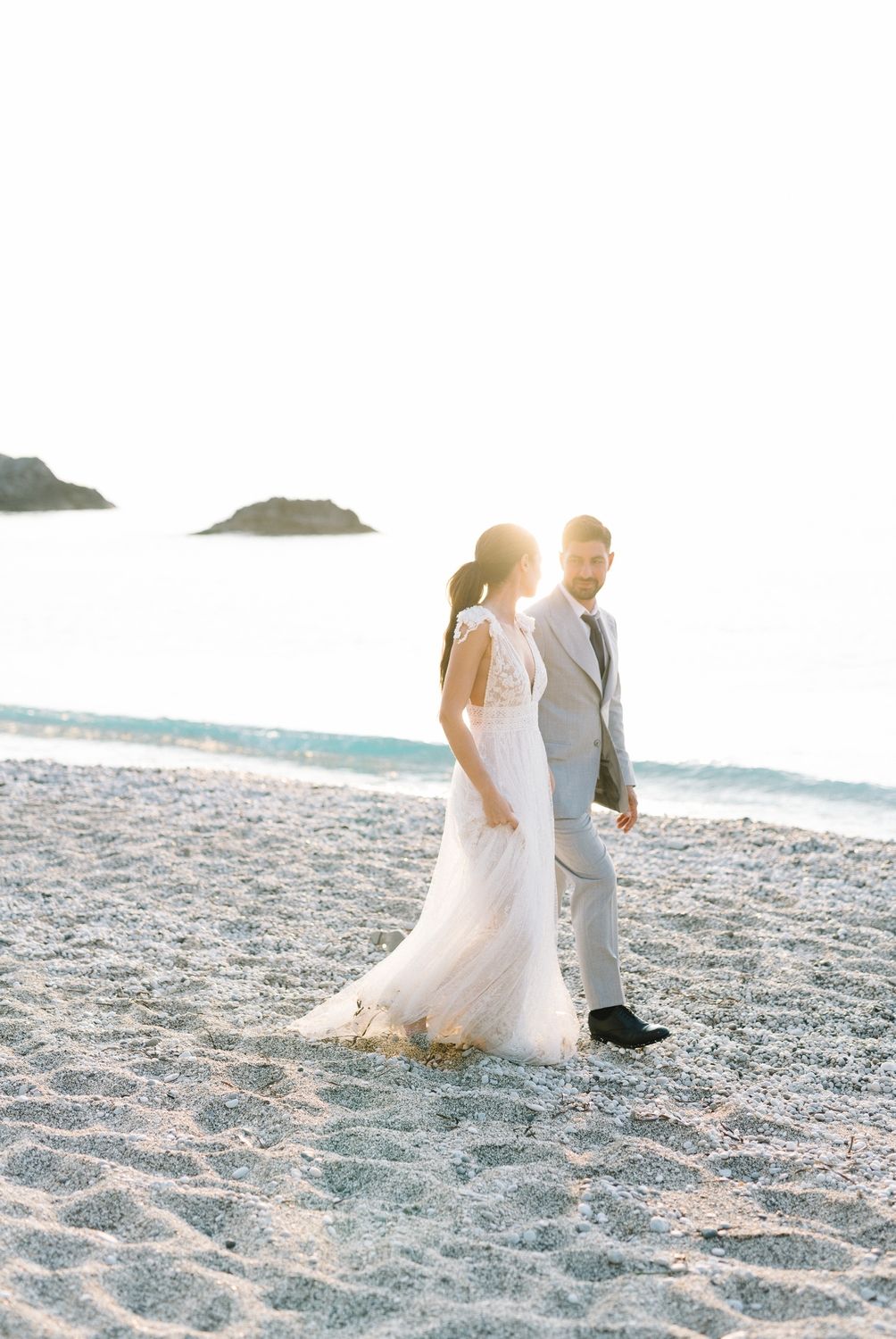 Sunlit beach wedding portrait with couple standing on sand against ocean backdrop.