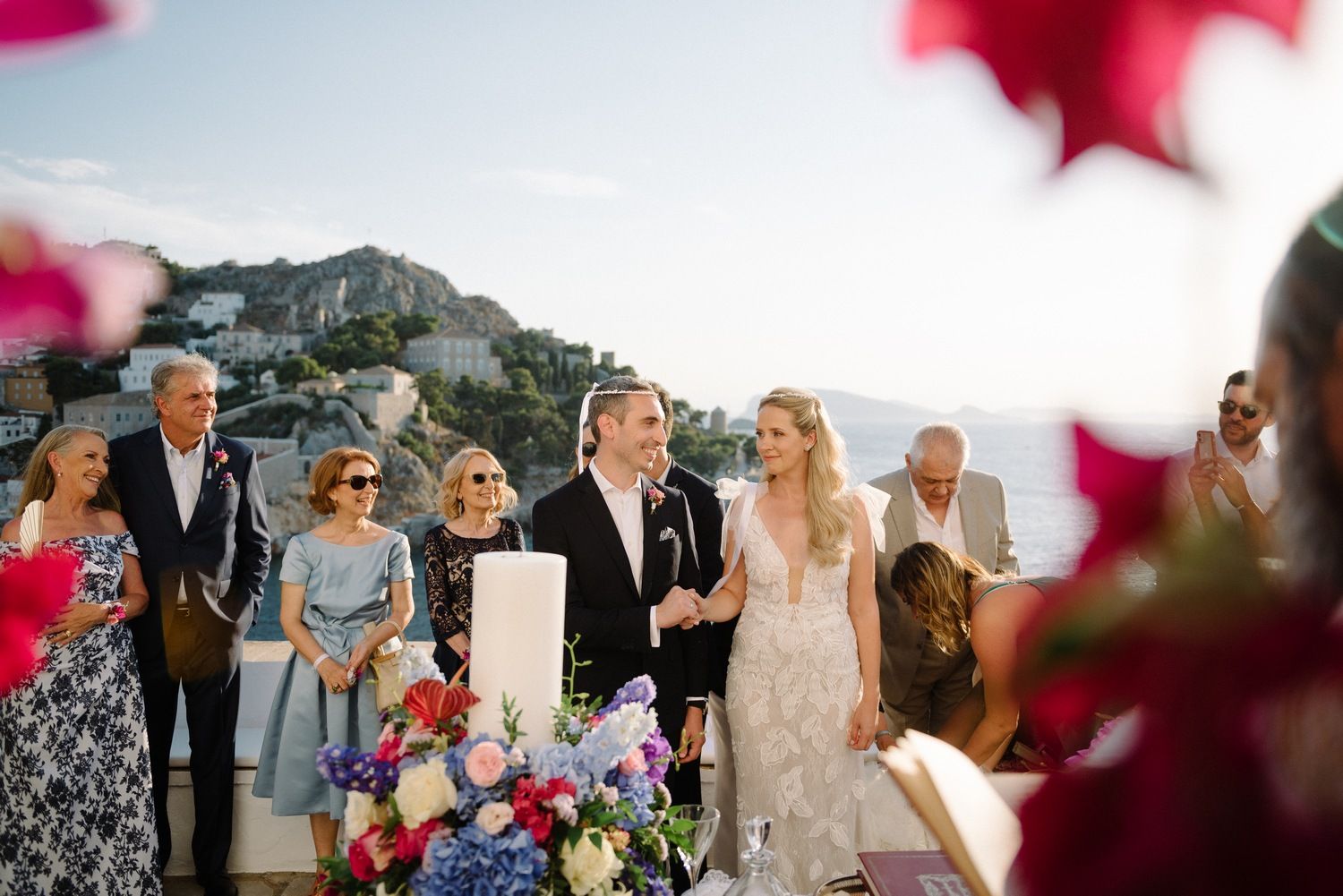 An outdoor wedding ceremony with guests seated overlooking a Mediterranean coastal landscape.