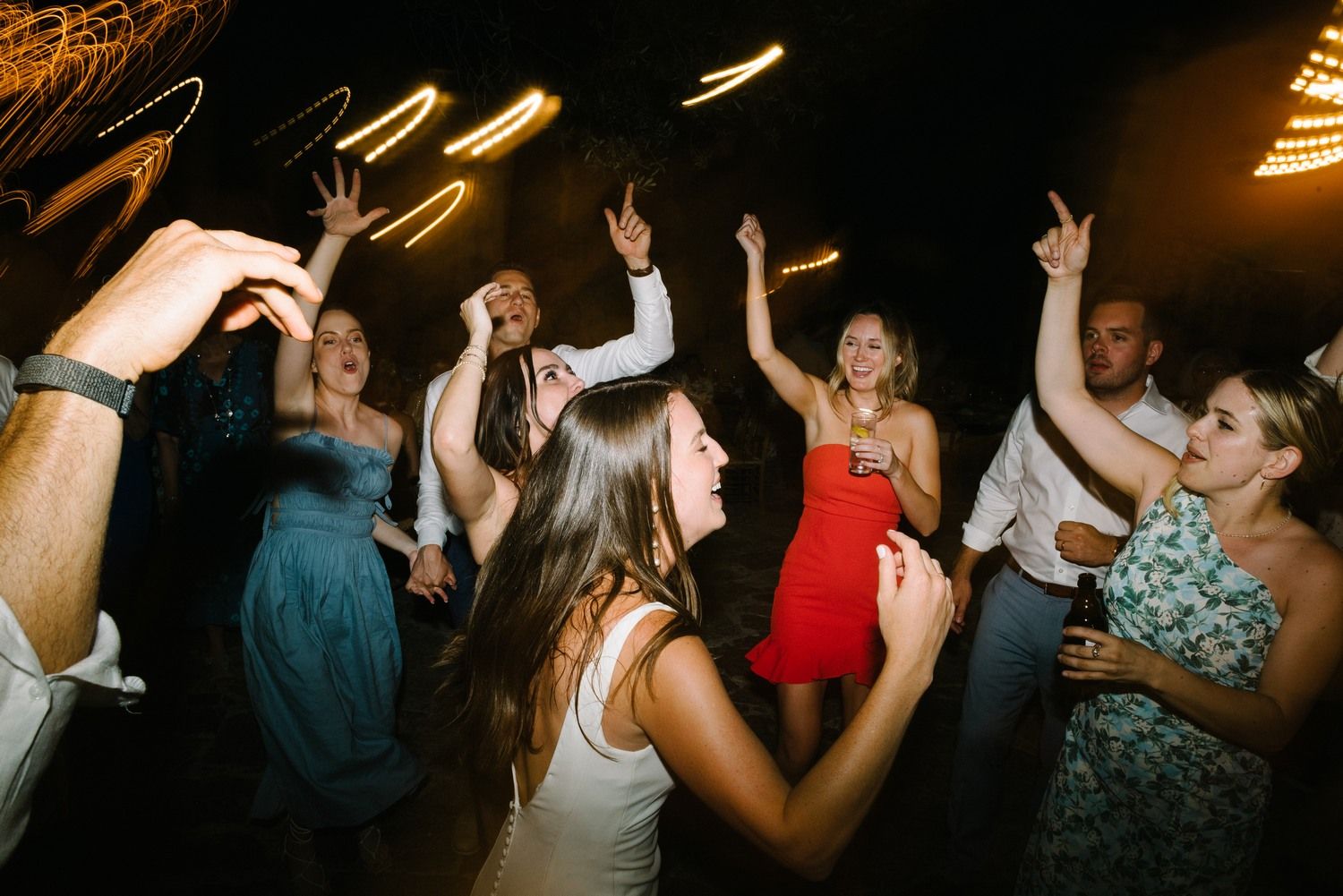 Party guests dancing enthusiastically under dim lighting at a reception.
