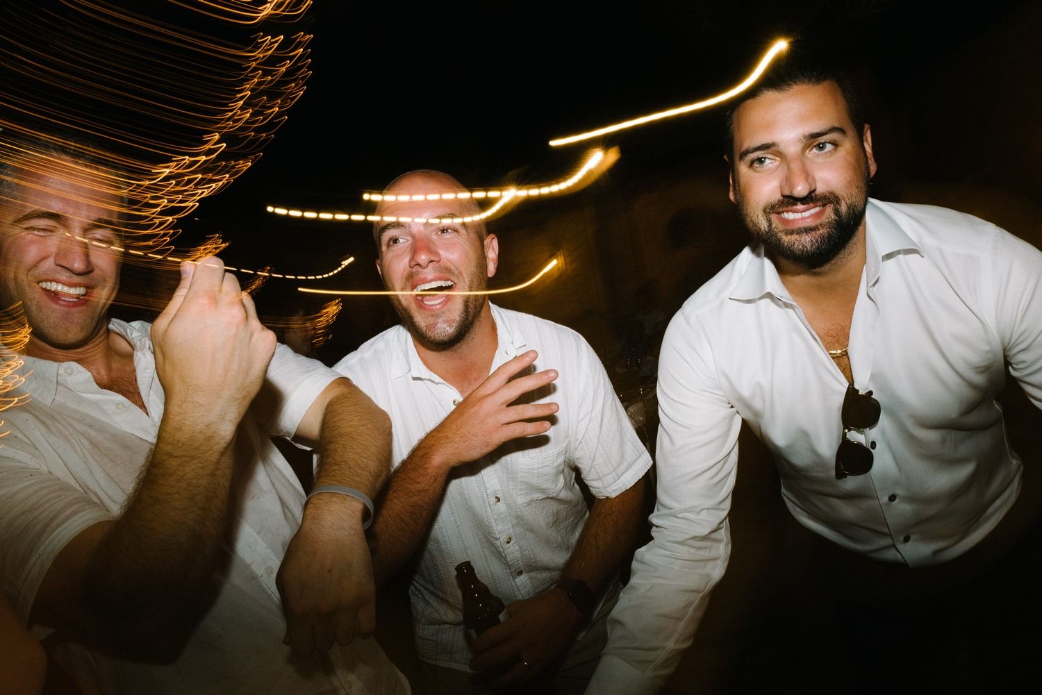 Three partygoers laughing and posing together under ambient lighting at an evening celebration.