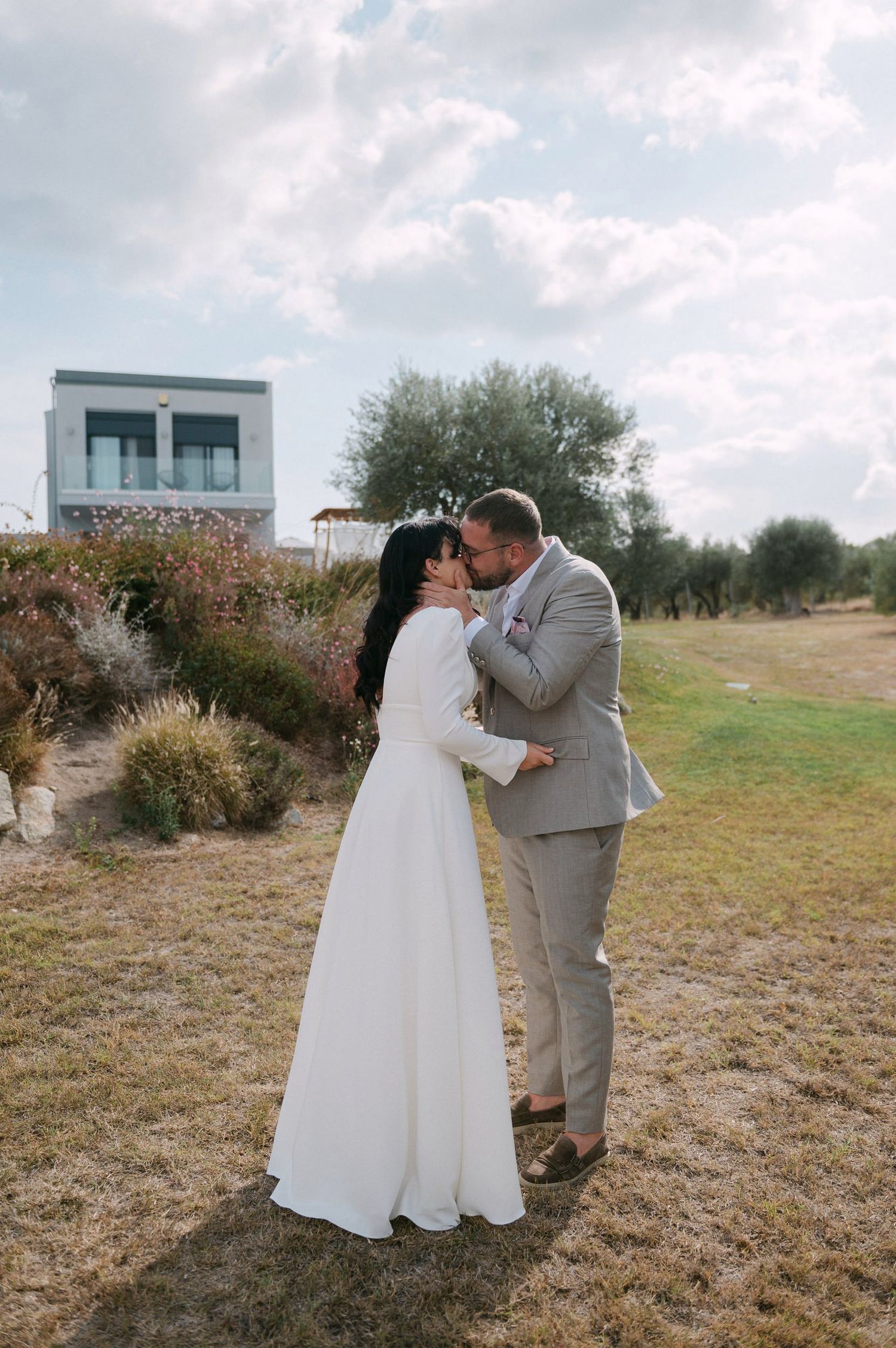 A romantic wedding couple shares tender moments in a rustic outdoor setting with natural landscaping.
