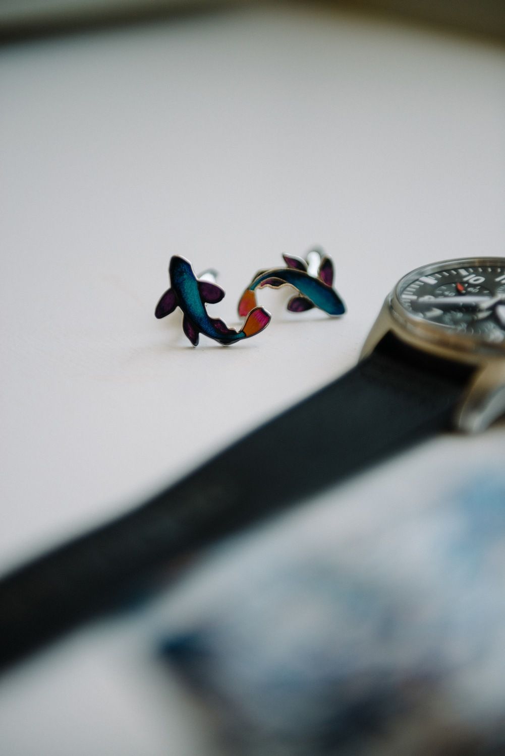 Decorative fish-shaped cufflinks displayed next to a watch strap.
