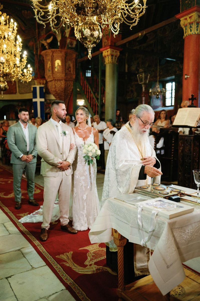 Orthodox wedding ceremony in progress with priest conducting service under grand chandeliers.