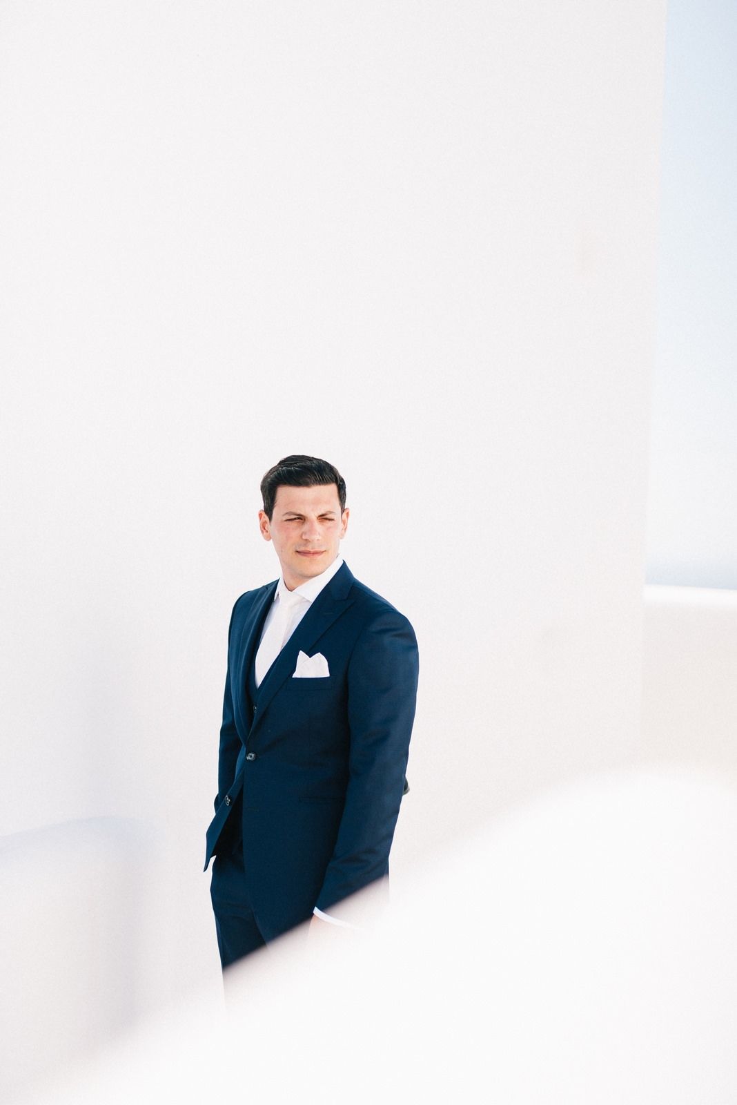 A formal portrait of someone in a navy suit against a minimalist white background.