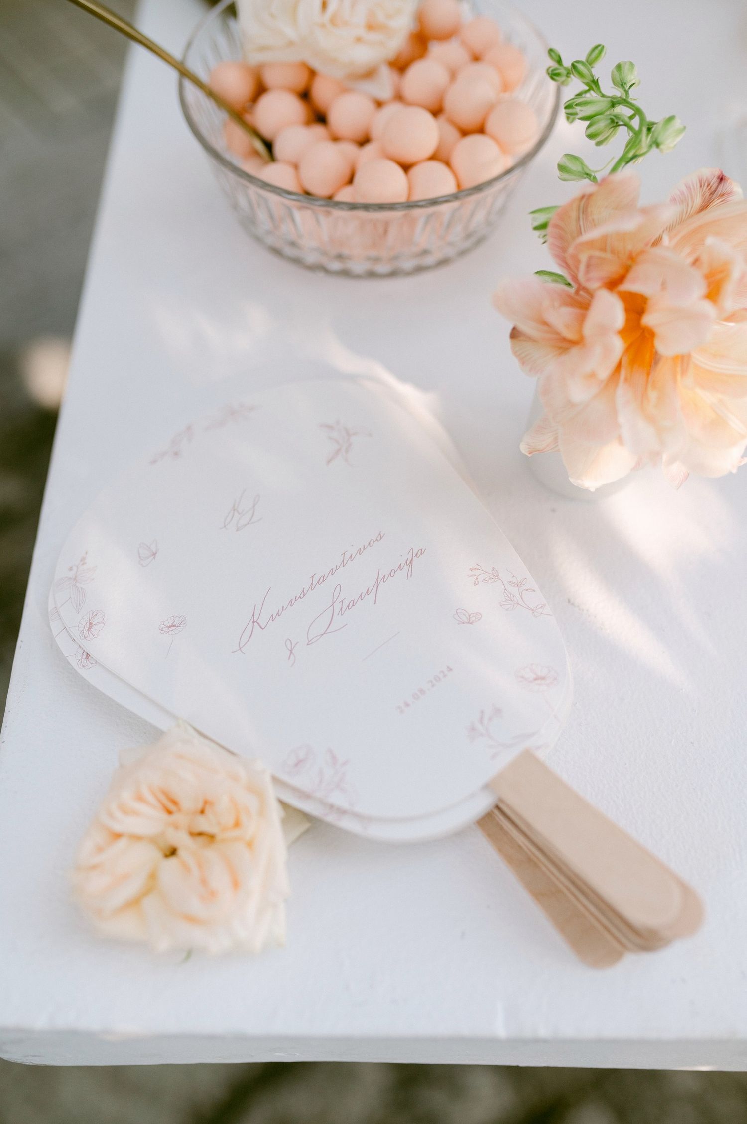Elegant wedding stationery with peach flowers and candies arranged on a white surface in soft natural light.