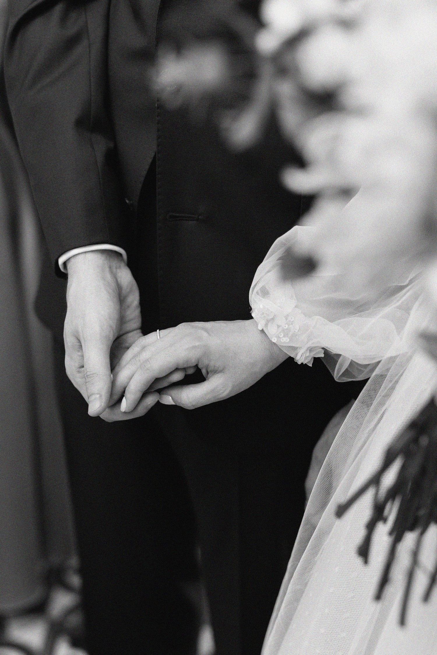 Black and white close-up photograph of a tender moment during a wedding ring exchange ceremony.