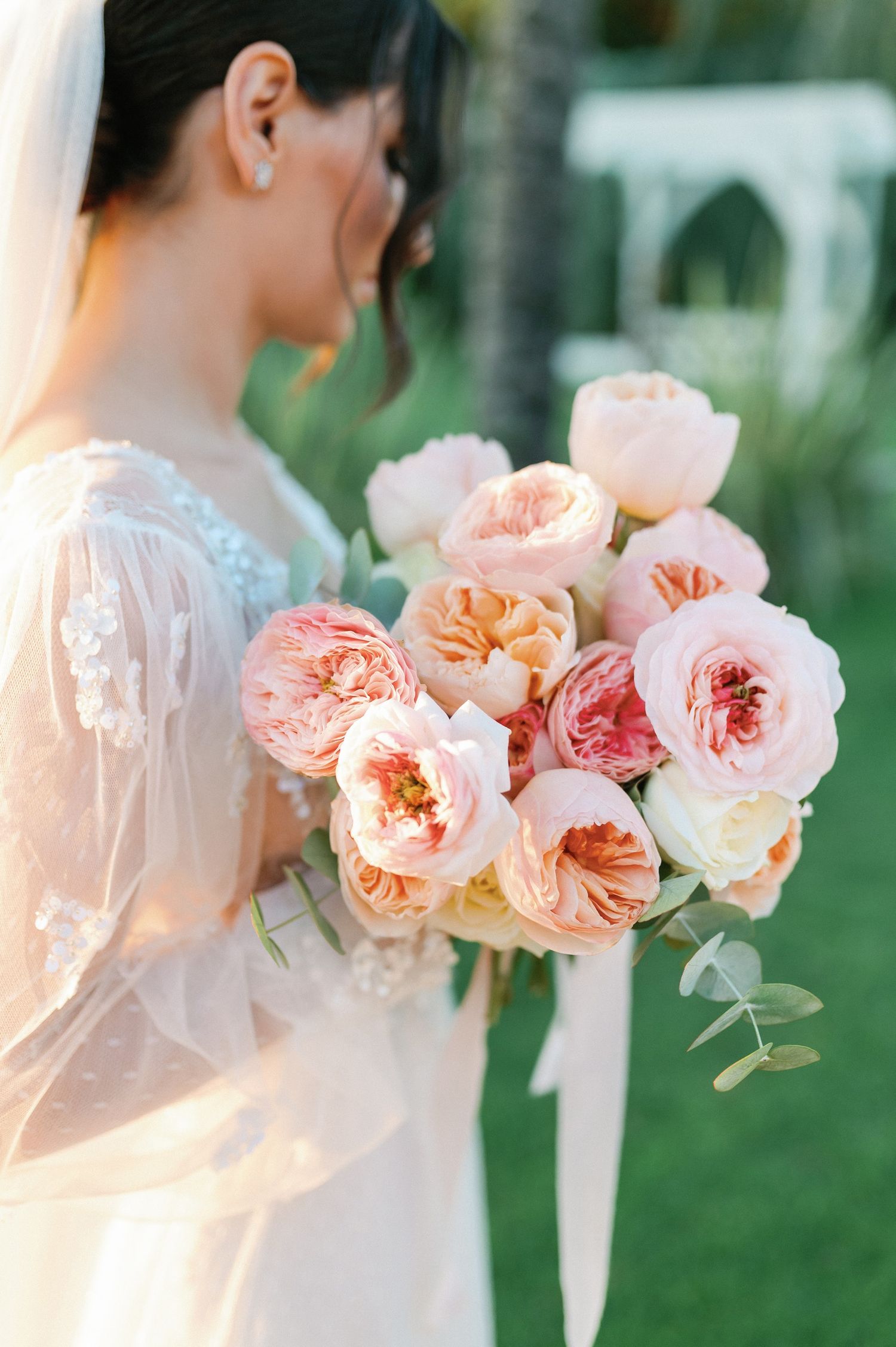 A delicate bouquet of peach and pink garden roses with soft greenery against a dreamy outdoor background.