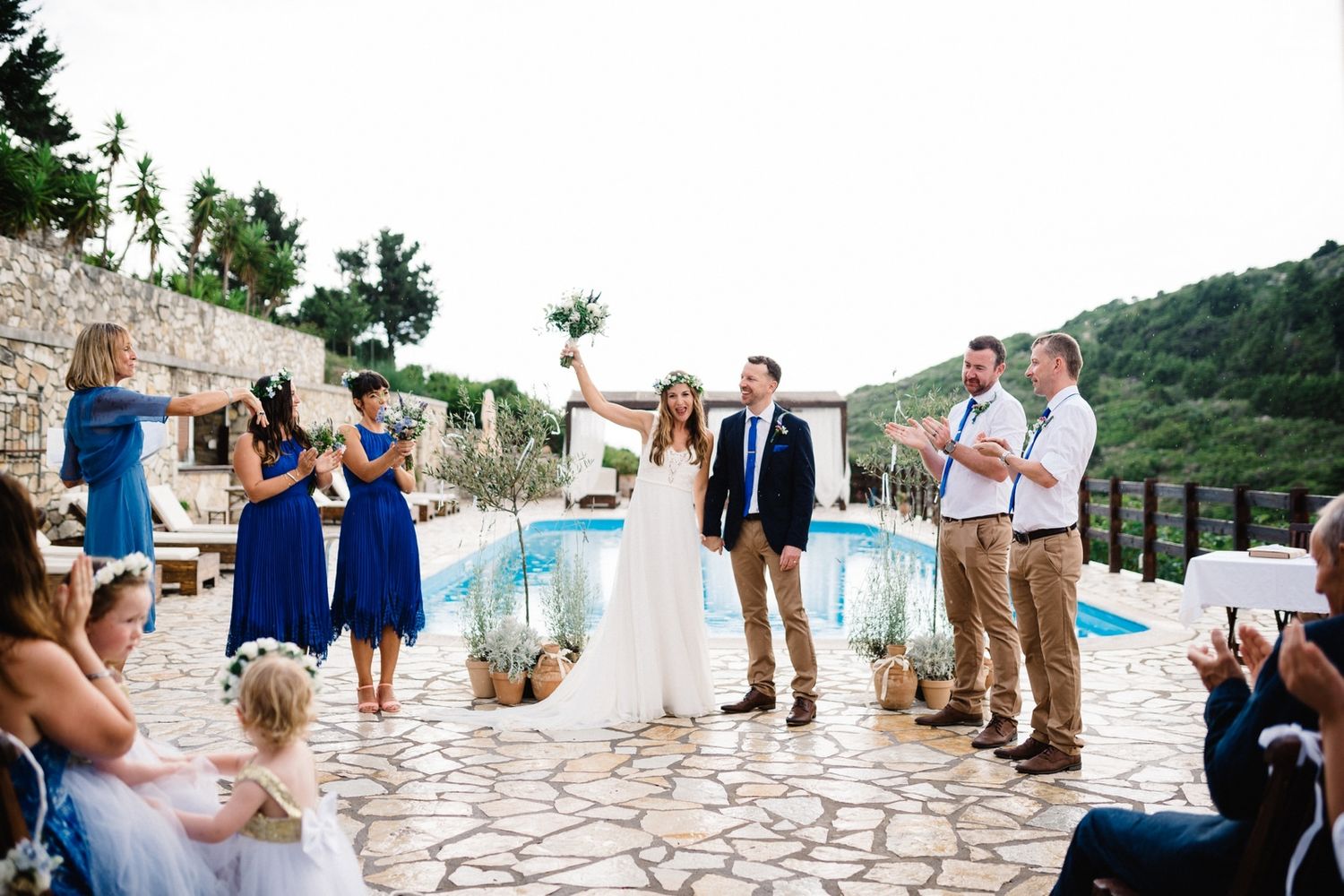 Destination wedding ceremony with guests watching couple against Mediterranean-style poolside setting.