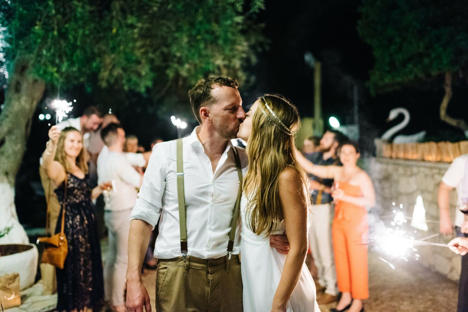 Newlyweds share an intimate moment during their sparkler exit celebration at night.