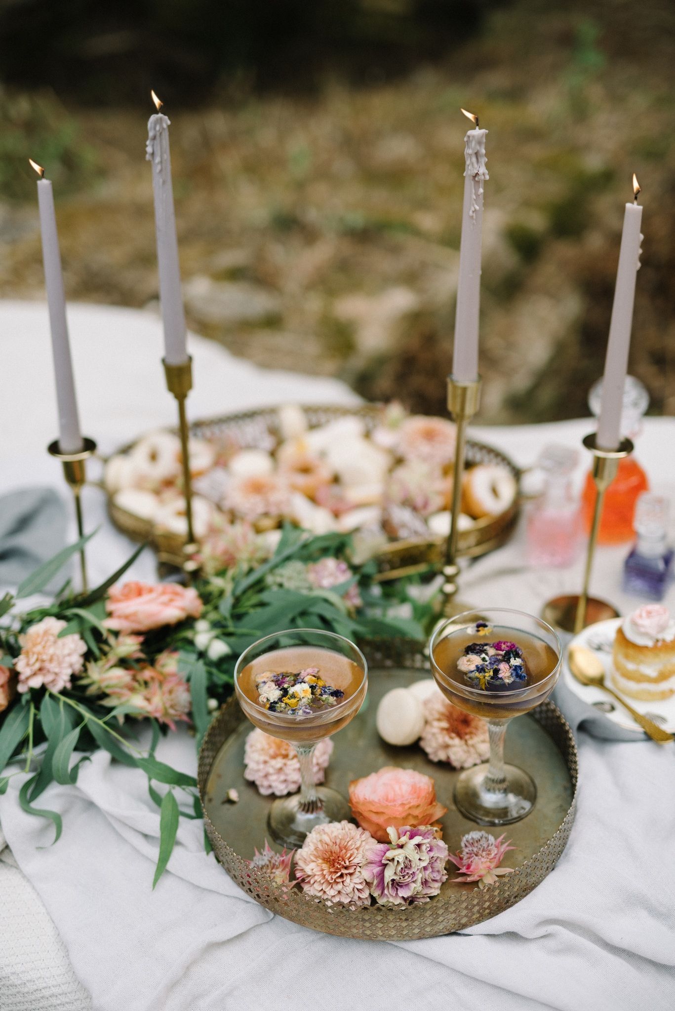 Elegant table setting with white candles, pink flowers and greenery on white tablecloth.