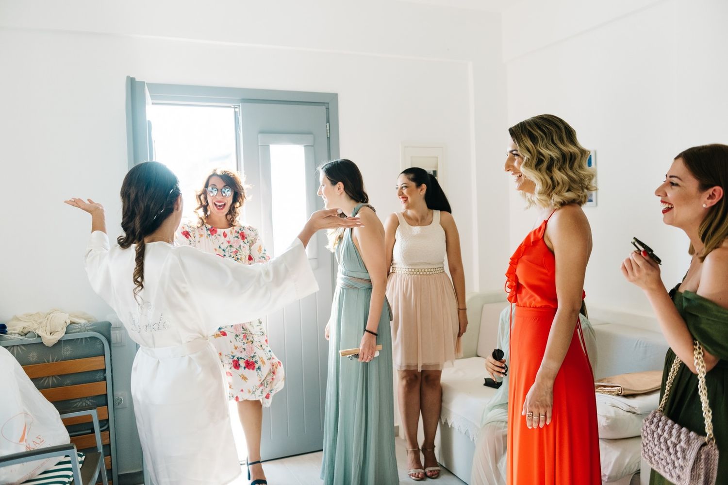 Bridesmaids in colorful dresses gather around a bride in white during wedding preparations.