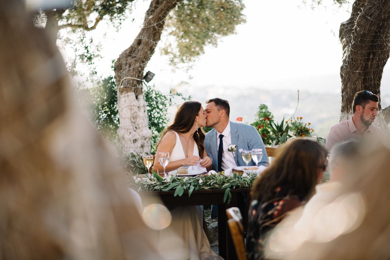 A wedding couple sharing a romantic moment under trees at an outdoor reception.