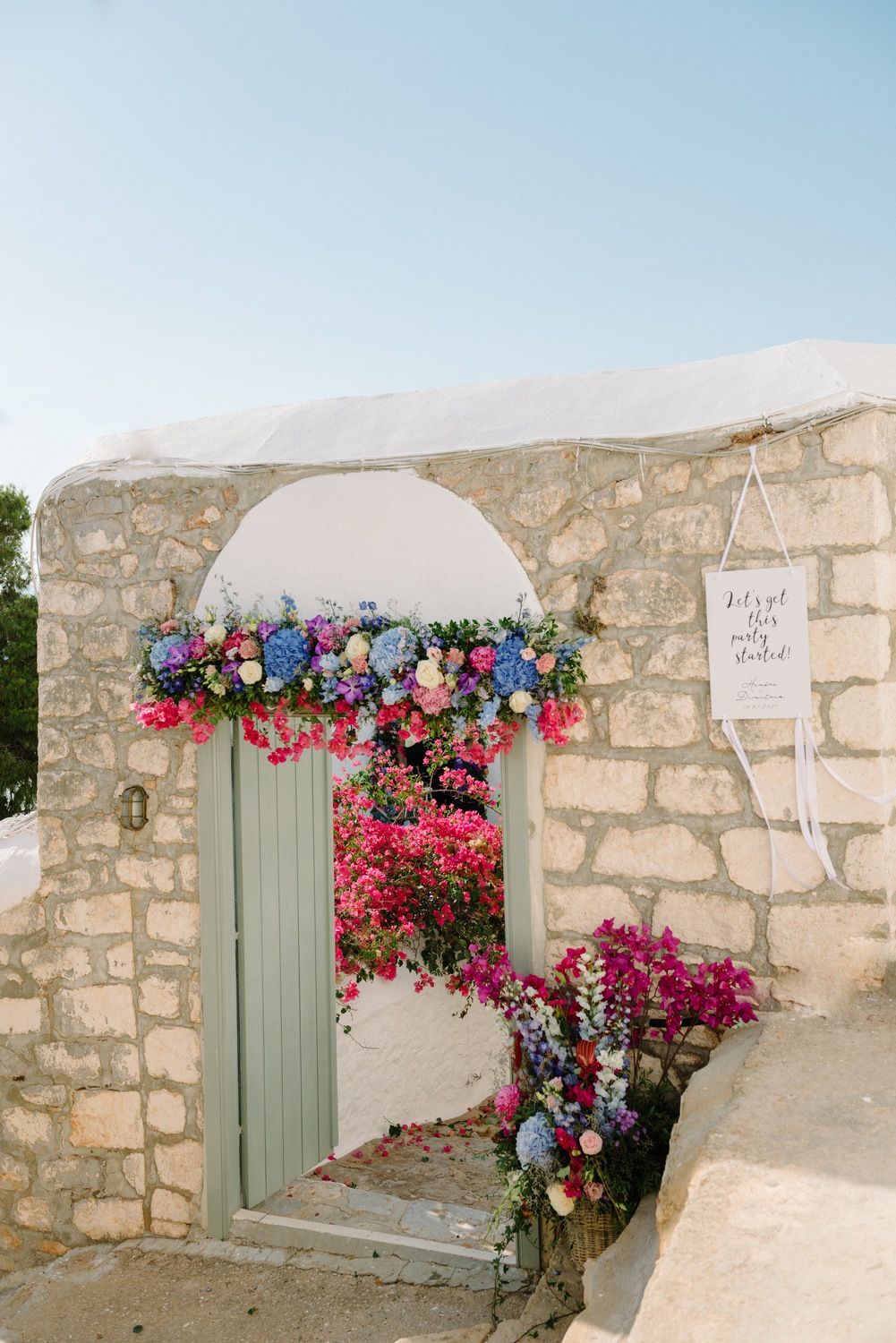 Stone archway decorated with pink and blue flowers against white Mediterranean architecture.