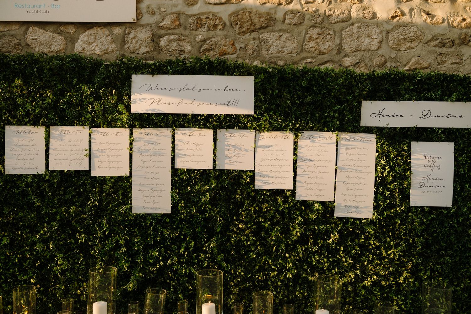 Wedding seating chart displayed on green hedge wall with white paper cards.