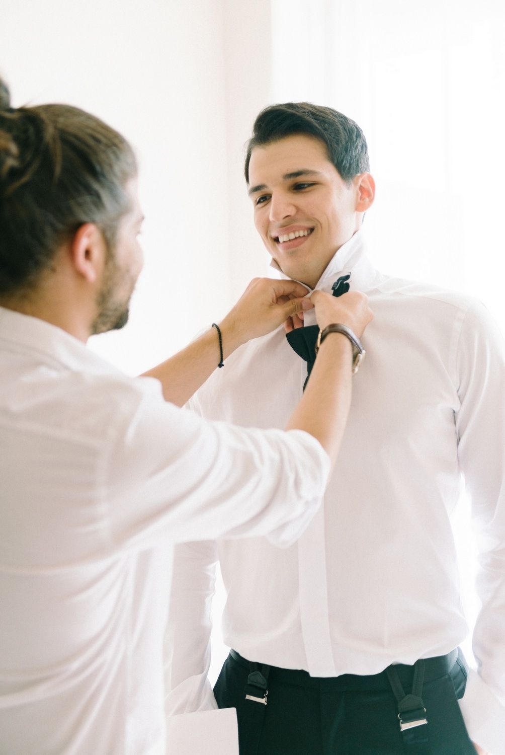 Two people in formal wear adjusting tie and suspenders before an event.