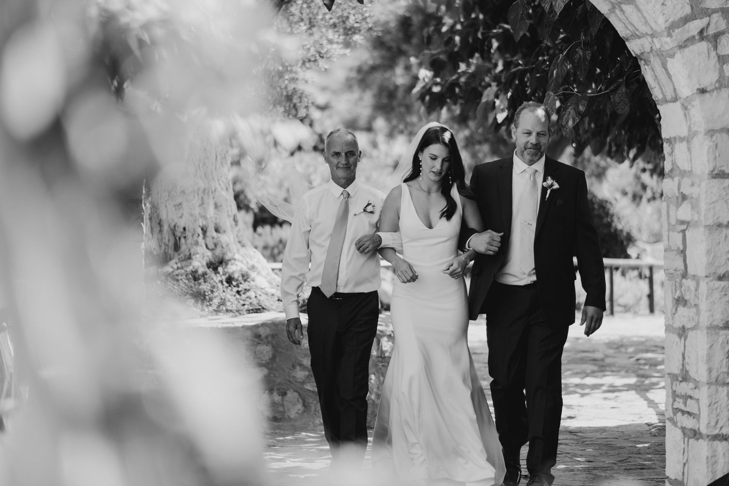 Black and white capture of a wedding ceremony entrance through a stone archway.