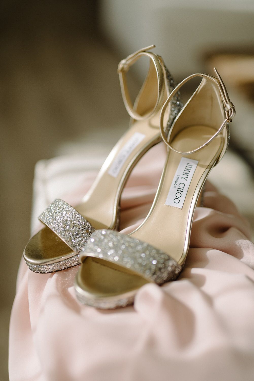 Glittering Jimmy Choo bridal shoes with sparkly straps displayed on pink fabric.