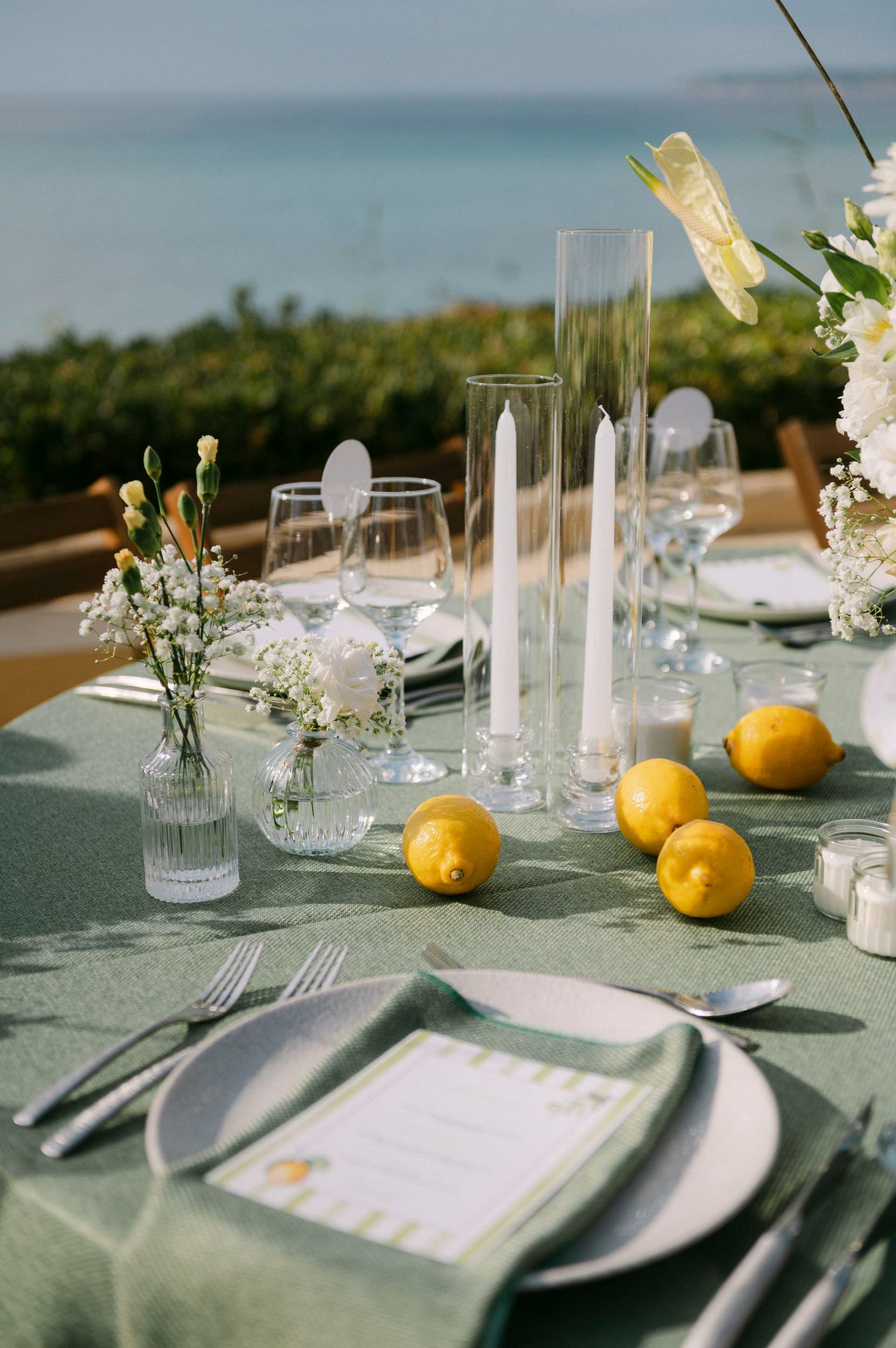 Elegant wedding table settings with fresh lemons and delicate white flowers on a sage green tablecloth in natural light.
