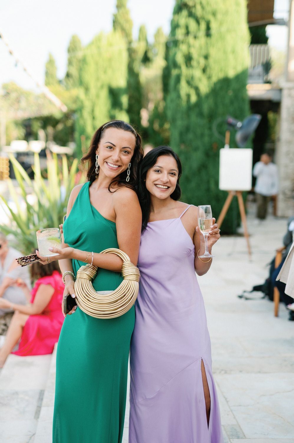 Two friends in green and purple dresses laugh and pose together at an outdoor event.