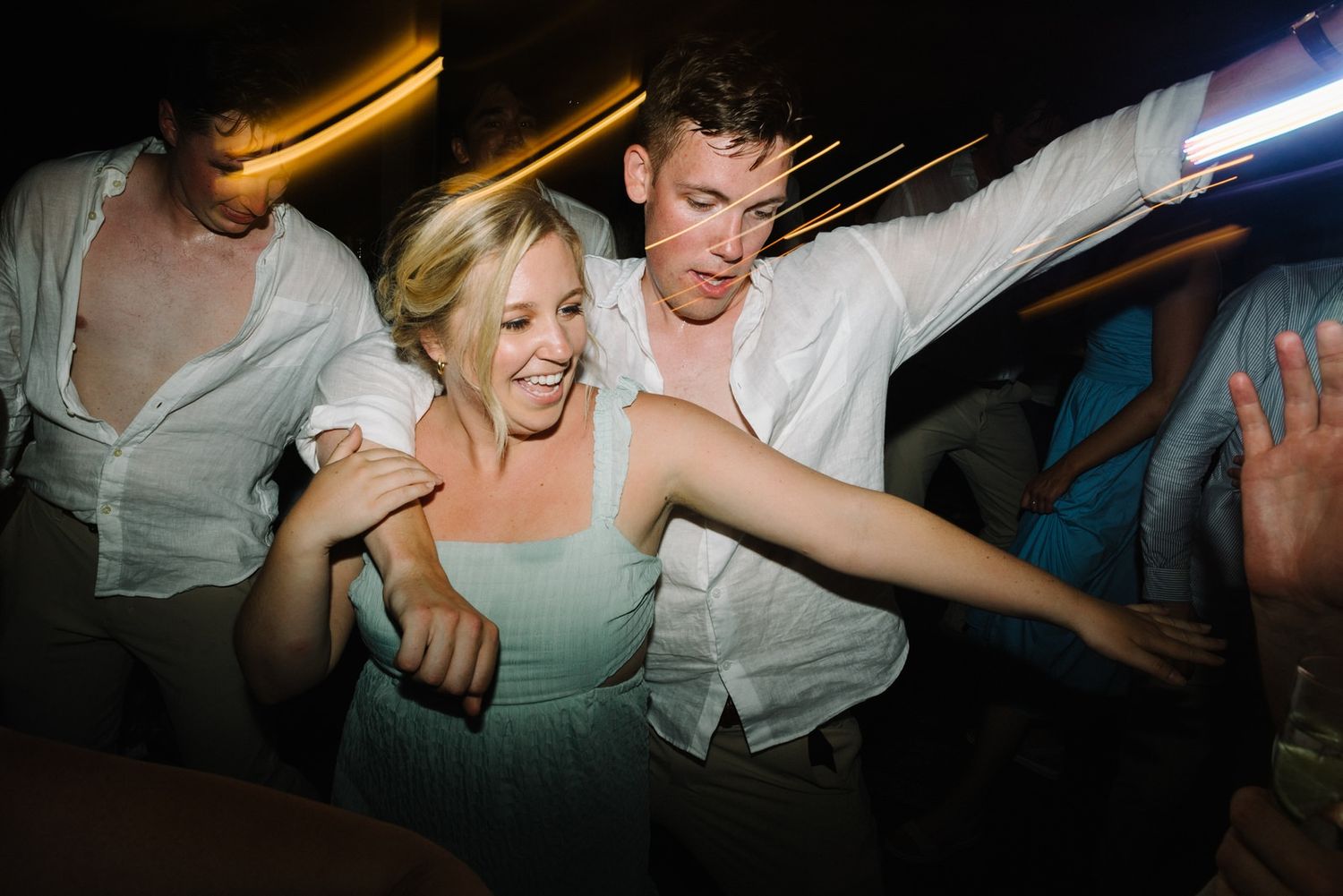 Wedding guests dance enthusiastically in a dimly lit venue.