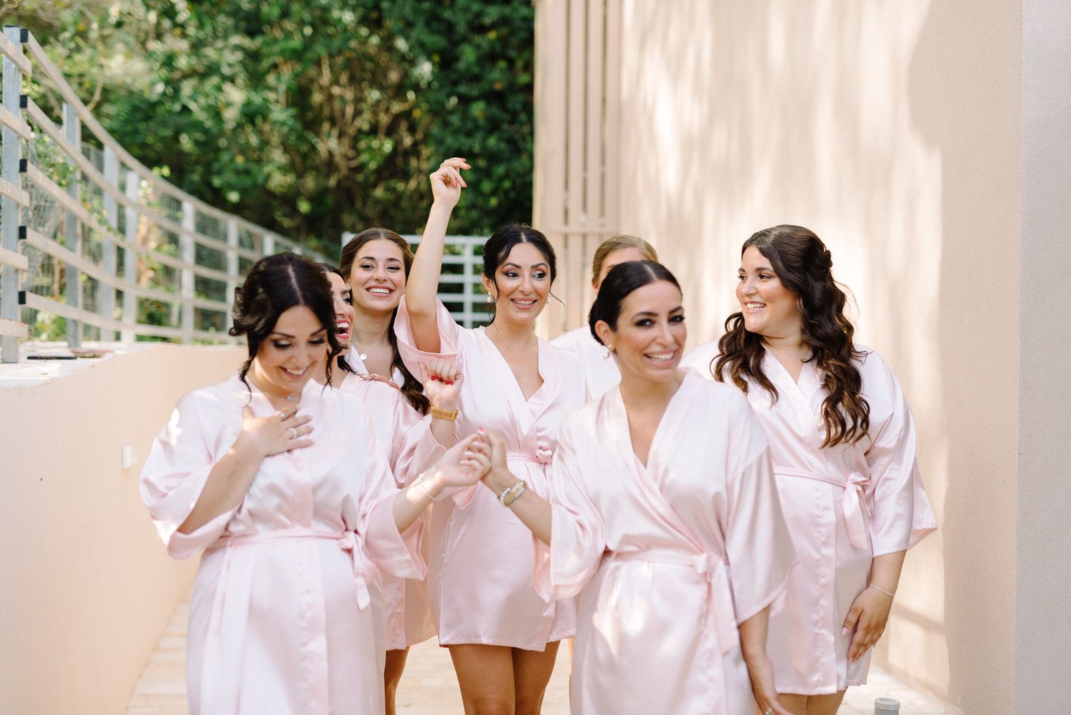 Cheerful bridal party in pink robes laughing together during pre-wedding preparations.