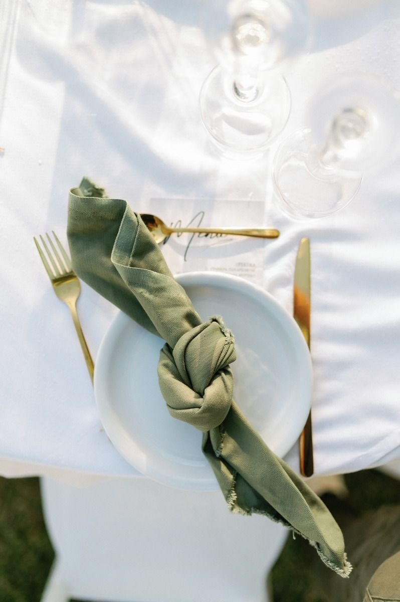 Artistically folded sage green napkin with gold cutlery on white plate at wedding place setting.