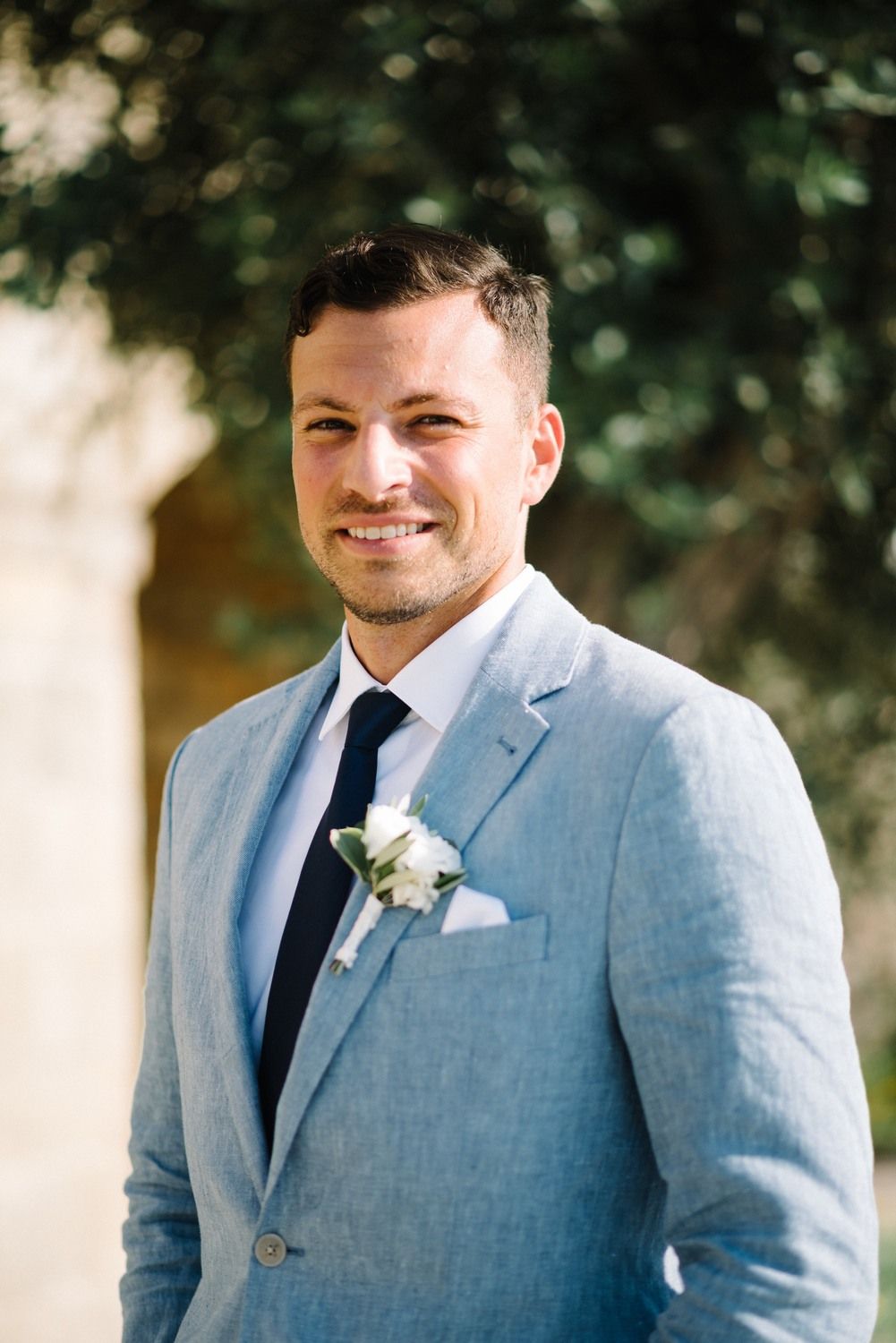 Close-up of groom smiling in light blue suit with white boutonniere.